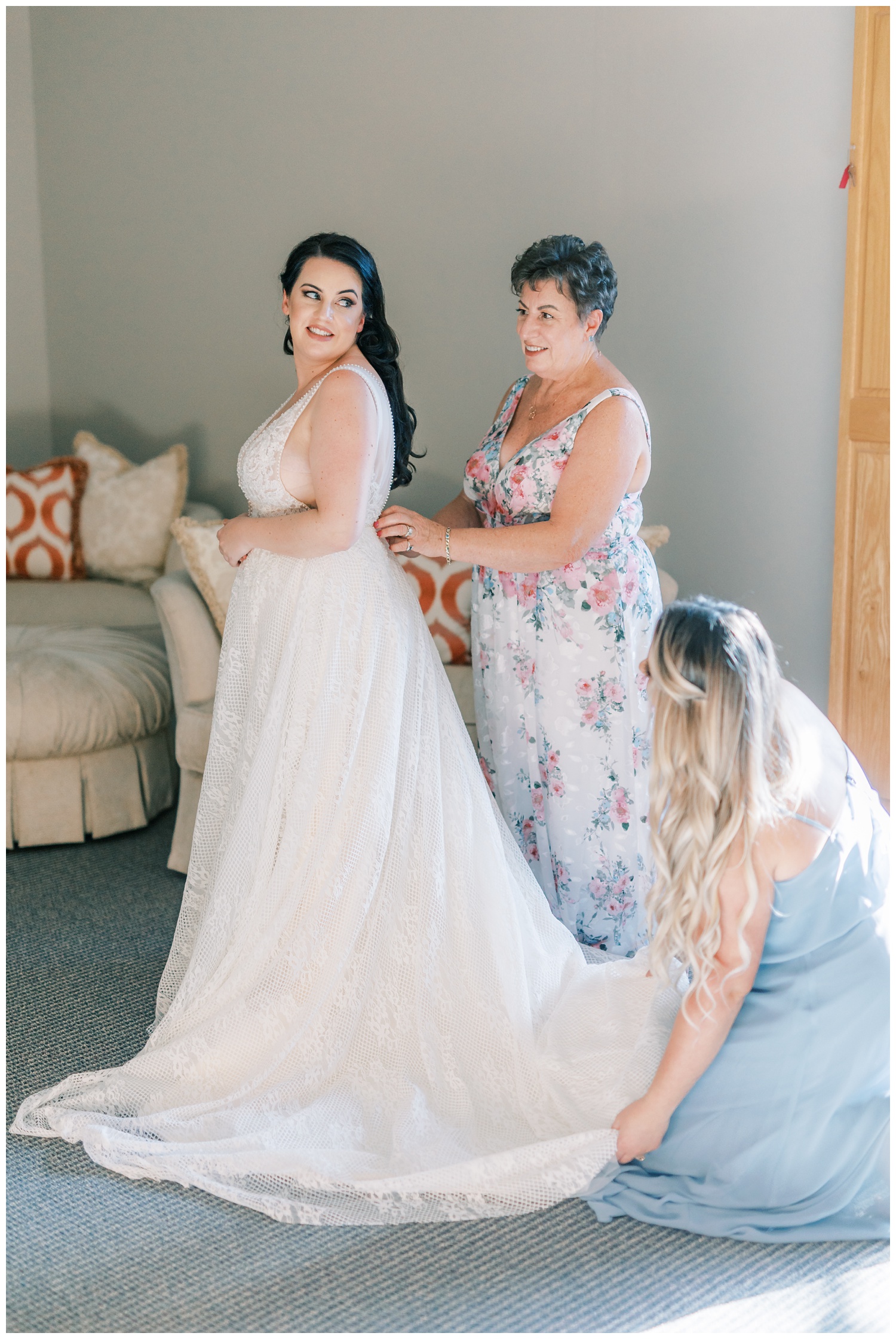 Mother and bridesmaid helping bride put her dress on